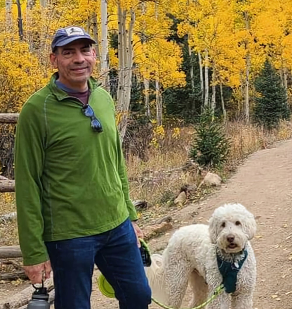 A picture of Ed Frank walking outside with his dog, with fall leaves in the background.
